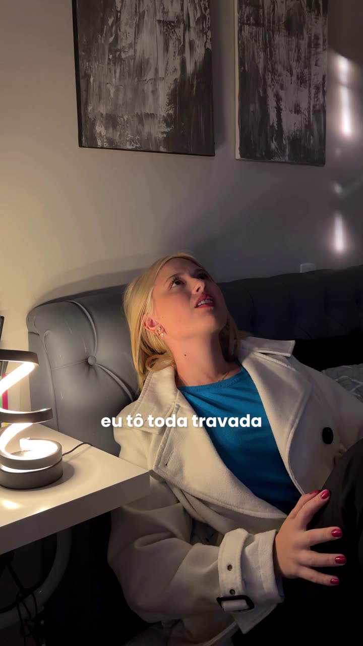 Mulher de casaco reclinada no sofá à noite, com expressão de desconforto, representando a sensação de corpo travado e rígido no fim do dia no inverno