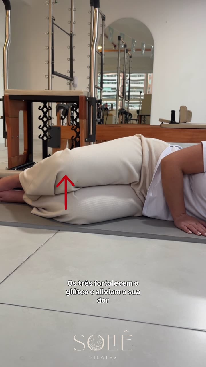 Instrutora da Soliê deitada de lado no tapete, com os dois joelhos dobrados e os pés juntos, abrindo o joelho de cima em rotação externa enquanto mantém a pelve imóvel. Uma seta vermelha aponta para o joelho que se abre.